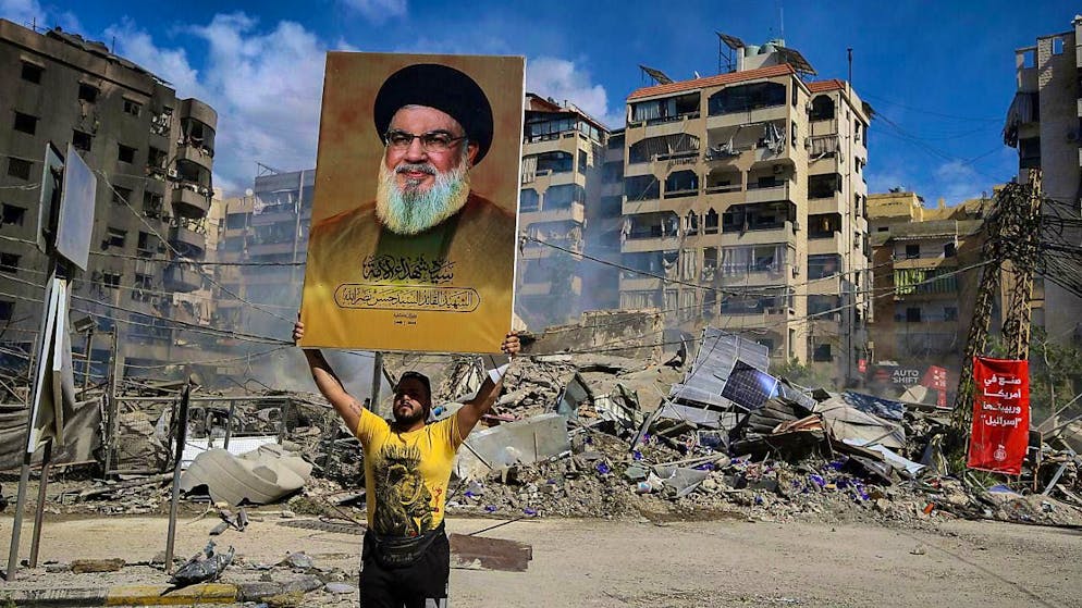 A pro-Iranian Hezbollah supporter holds up a poster of slain Hezbollah Secretary General Nasrallah in front of a building destroyed in an Israeli airstrike on a southern suburb of Beirut. (archive picture)