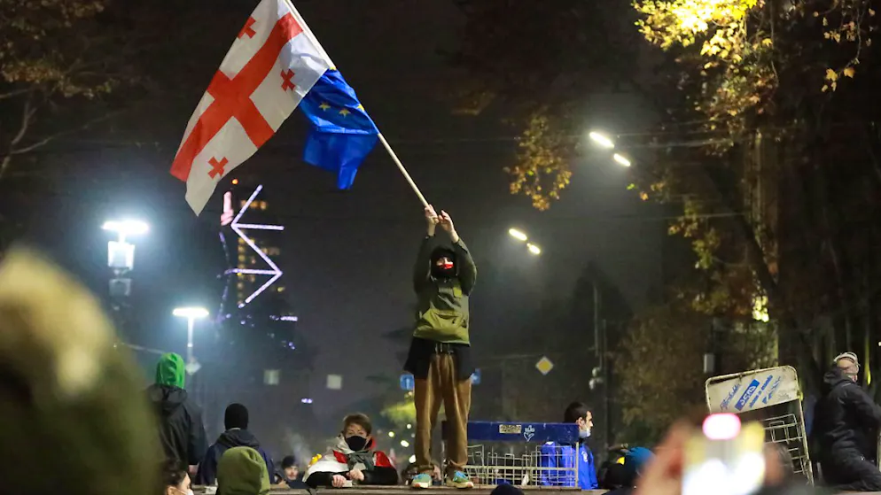 Ein Demonstrant steht mit georgischen National- und EU-Flaggen während einer Kundgebung vor dem Parlamentsgebäude in Tiflis.