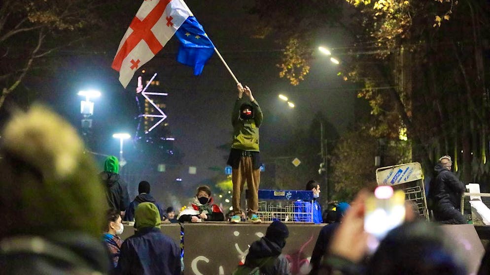 dpatopbilder - A demonstrator stands with Georgian national and EU flags during a rally in front of the parliament building in Tbilisi. Photo: Zurab Tsertsvadze/AP/dpa