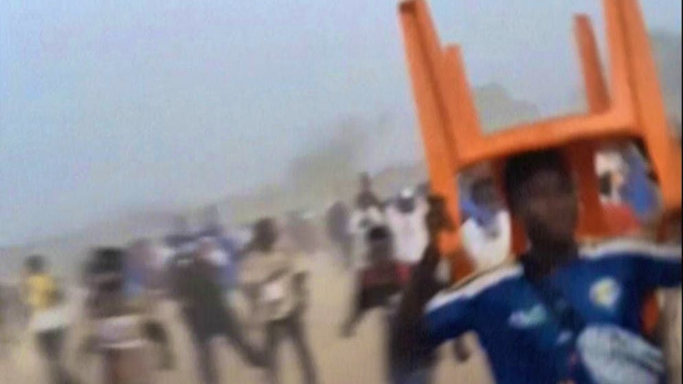 A man holds a chair over his head as a shield. Tumult and mass panic break out in Nzerekore after a football match