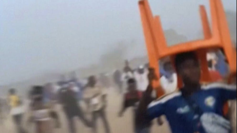 Ein Mann nimmt als Schutzschild einen Stuhl über den Kopf. In Nzerekore herrscht nach einem Fussballspiel Tumult und Massenpanik bricht aus