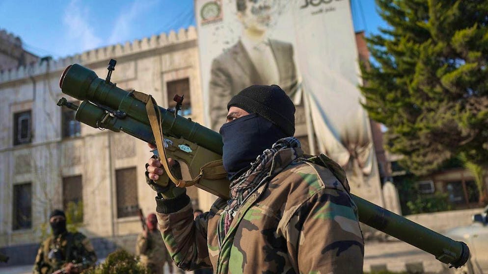 A Syrian opposition fighter holds a rocket launcher in front of the provincial government office, with a picture of Syrian President Bashar Assad riddled with bullets on its facade, after the takeover of the city. Photo: Ghaith Alsayed/AP/dpa