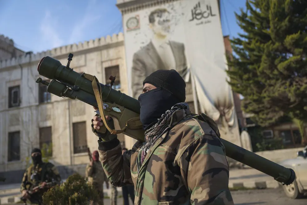Un combattente dell'opposizione siriana tiene un lanciarazzi davanti all'ufficio del governo provinciale, dove l'immagine del presidente siriano Bashar Assad è crivellata di proiettili sulla facciata, all'indomani della conquista di Hama da parte dell'opposizione, venerdì 6 dicembre 2024.
