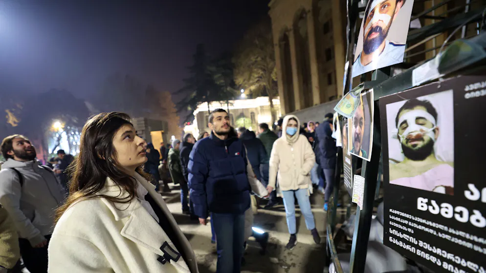 Eine Frau betrachtet Bilder von Personen, die Berichten zufolge von der Polizei geschlagen wurden und die von Demonstranten am Metallrahmen des Weihnachtsbaumes vor dem Parlament im Zentrum von Tiflis befestigt wurden.
