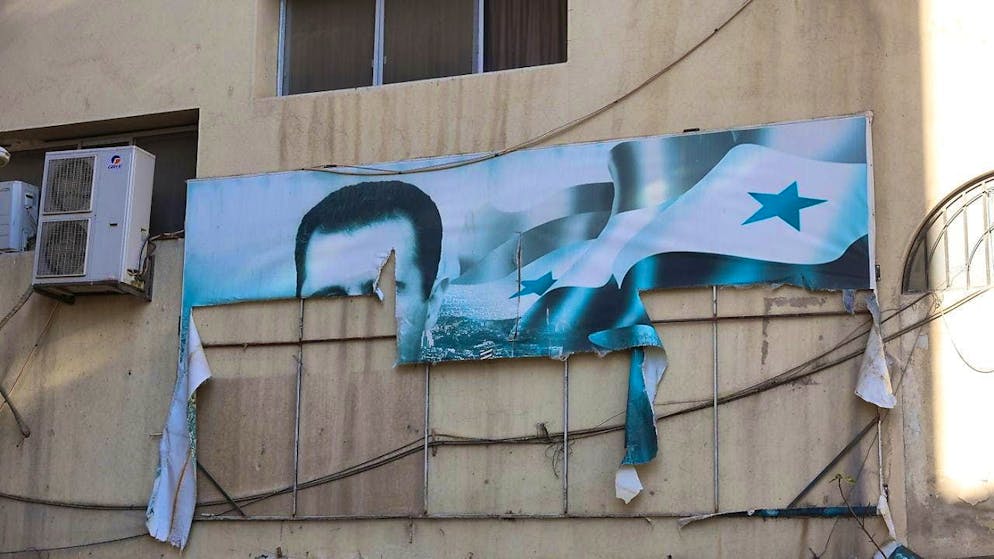 A torn banner shows the photo of ousted Syrian ruler Bashar al-Assad.