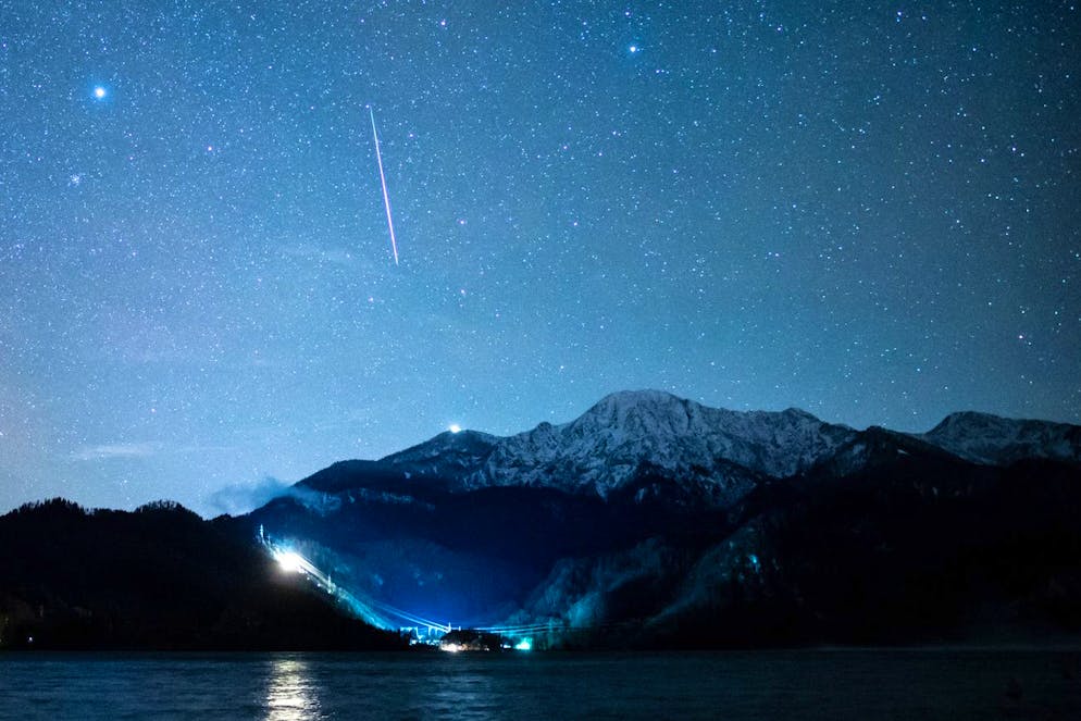 Eine Sternschnuppe ist während des Geminiden-Meteteorstroms am Sternenhimmel über dem Kochelsee (Bayern). Die Geminiden sind der stärkste Meteorstrom des Jahres.