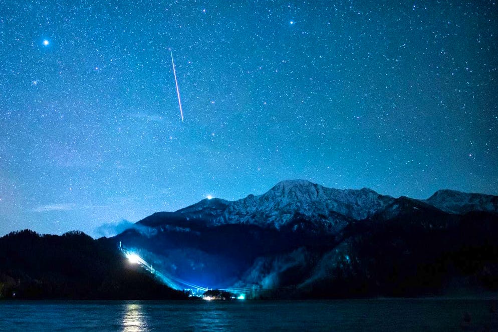Una stella cadente è visibile nel cielo stellato sopra il lago di Kochel (Baviera) durante il flusso di meteore Geminidi. Le Geminidi sono il flusso meteorico più forte dell'anno.