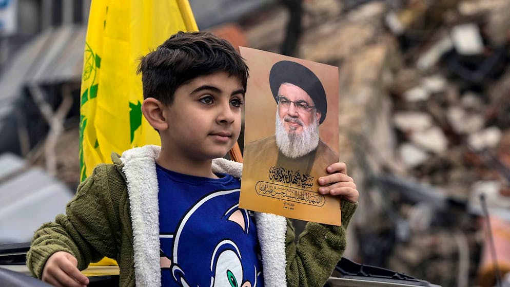 ARCHIV - Ein vertriebener Junge, der ein Bild des getöteten Hisbollah-Führers Hassan Nasrallah hält, kehrt mit seiner Familie zurück, nachdem eine Waffenruhie zwischen Israel und der Hisbollah in Kraft getreten ist. Foto: Bilal Hussein/AP/dpa