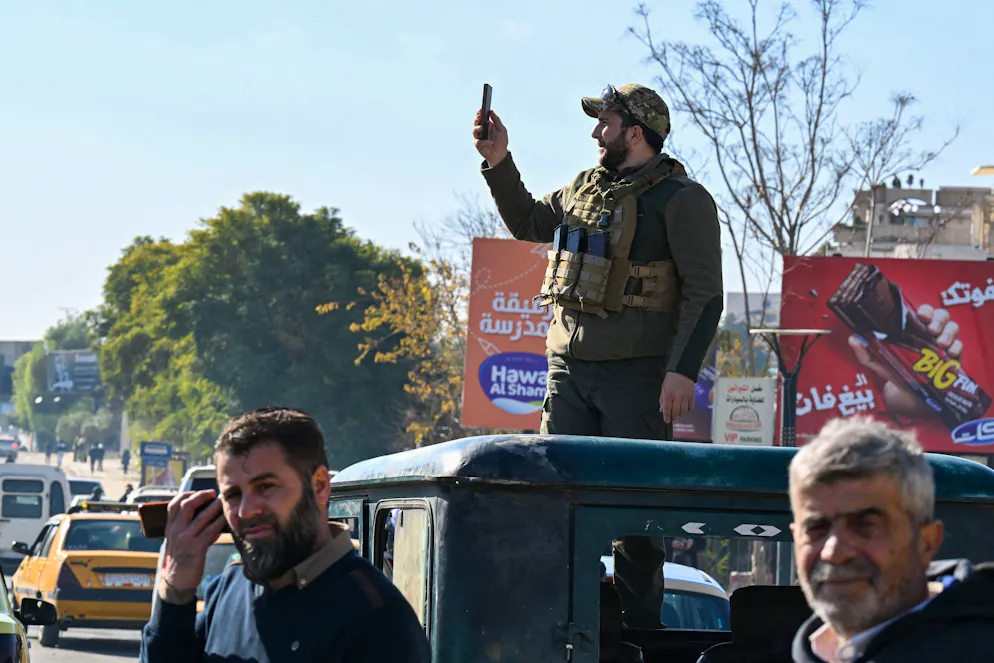 Un combattant rebelle prend des photos avec son téléphone alors que des étudiants syriens se rassemblent près du campus de l'université de Damas, dans la capitale syrienne, le 15 décembre 2024. Les rebelles islamistes ont pris Damas lors d'une offensive éclair le 8 décembre, chassant le président Bachar al-Assad et mettant fin à cinq décennies de régime Baas en Syrie.