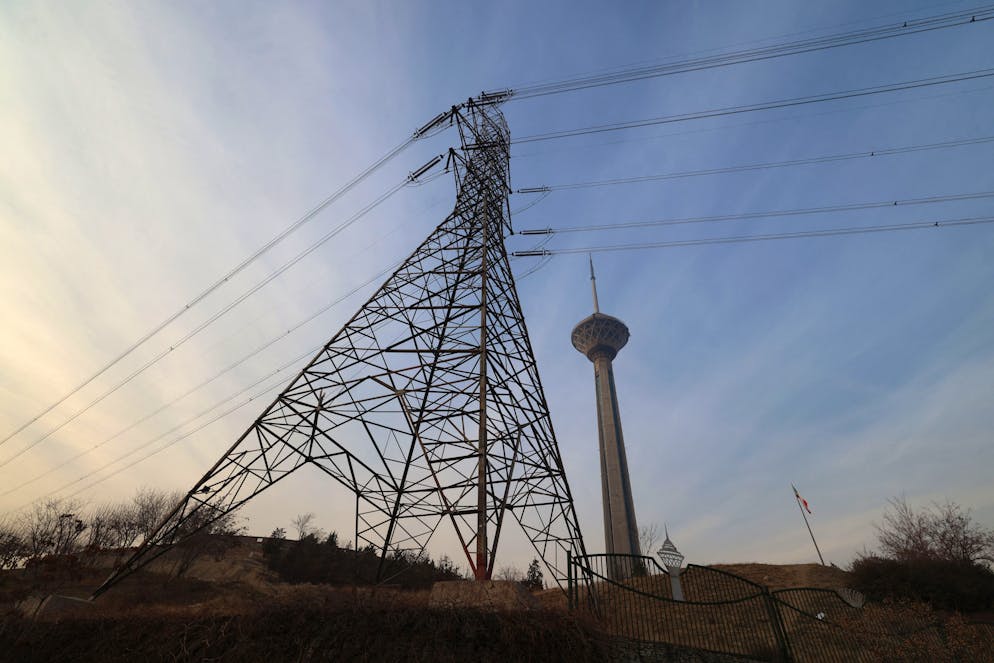 A picture shows an electricity transmission tower, with a view of the Milad Tower in Tehran on December 16, 2024. - Iran has suspended operations at several power plants over fuel shortages that have been intensified by rising demand during a spell of freezing weather. (Photo by ATTA KENARE / AFP)