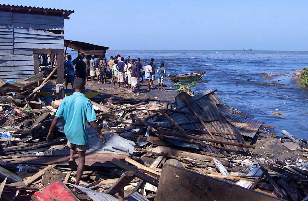 Des personnes marchent parmi les débris de leurs maisons détruites par les raz-de-marée sur les zones côtières de Colombo, Sri Lanka, dimanche 26 décembre 2004. Des vagues massives, apparemment déclenchées par des tremblements de terre océaniques, se sont abattues sur des villages côtiers dans une vaste zone du Sri Lanka dimanche, tuant au moins 300 personnes et en déplaçant 100 000 autres. (AP Photo/Eranga Jayawardena) Traduit avec DeepL.com (version gratuite)