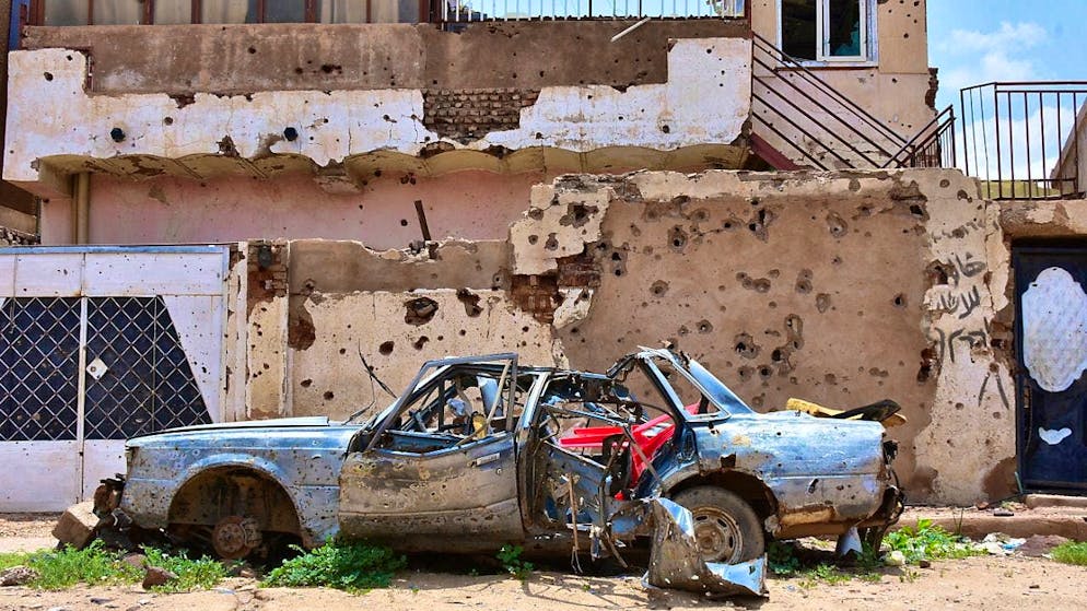 ARCHIVE - A destroyed car stands in front of a house full of bullet holes. Photo: Mudathir Hameed/dpa