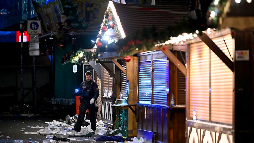 Ein Polizist untersucht den Tatort auf dem Weihnachtsmarkt. Foto: Heiko Rebsch/dpa
