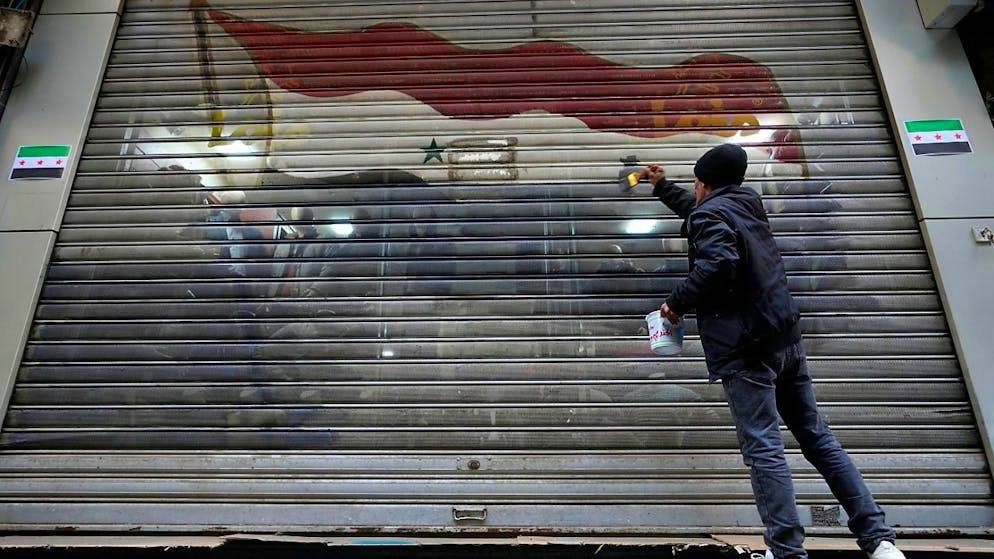 ARCHIV - Ein Mann entfernt die Farben der offiziellen Flagge der gestürzten Regierung von einem Türgeschäft. Foto: Hussein Malla/AP/dpa