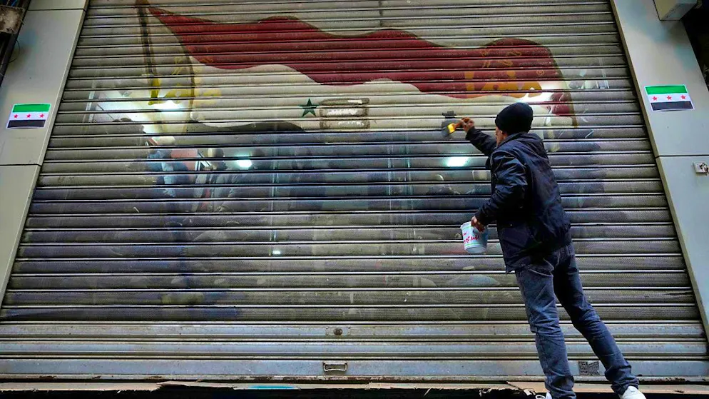 ARCHIVE - A man removes the colors of the official flag of the ousted government from a door store. Photo: Hussein Malla/AP/dpa