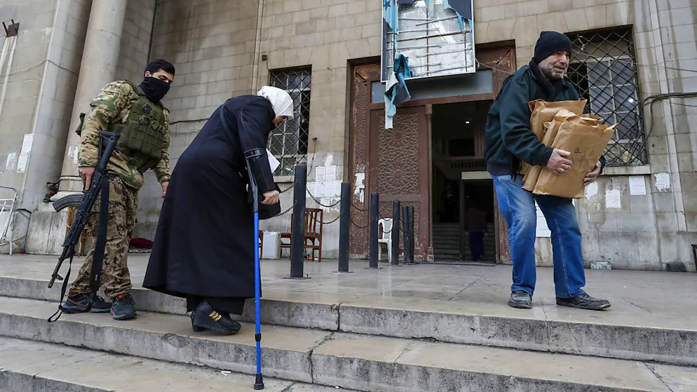 Sous une photo déchirée du président syrien évincé Bachar Assad, un combattant syrien aide une femme devant le palais de justice à Damas en Syrie lundi.