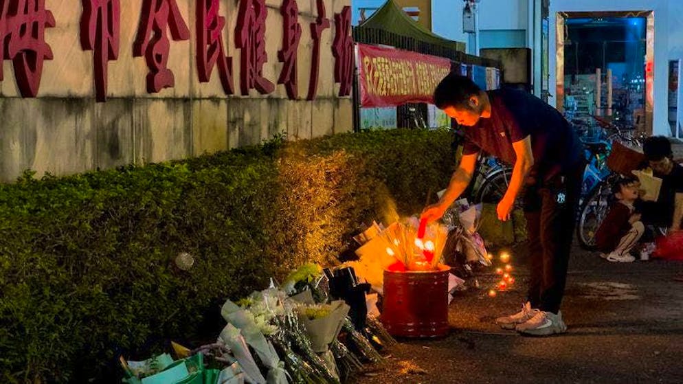 A man lights a candle placed in front of the Zhuhai People's Fitness Plaza, where a man deliberately rammed his car into people exercising at the sports center.