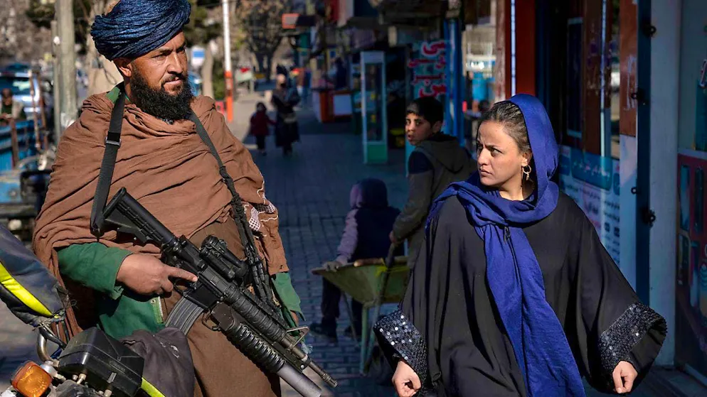 A Taliban fighter stands guard while a woman walks by. (symbolic image)