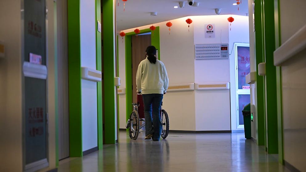 ARCHIV - Eine Altenpflegerin schiebt einen Rollstuhl in einem Flur. In China gibt es landesweit Projekte, in denen ehemalige Schulen oder Kindergärten in Pflegeheime umfunktioniert werden. Foto: Johannes Neudecker/dpa