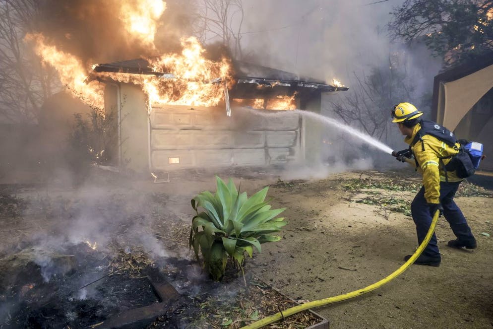 Inferno di fuoco a Los Angeles, migliaia di persona in fuga. Un vigile del fuoco della contea di Los Angeles cerca di spegnere un incendio da una struttura in fiamme durante l'incendio di Eaton ad Altadena, California
