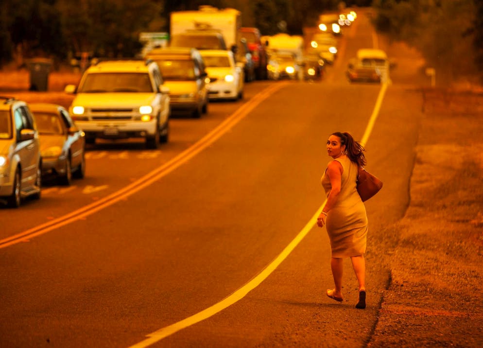 Wildfires in California: Thousands evacuated - Gallery. A woman walks along a street while the Thompson Fire burns