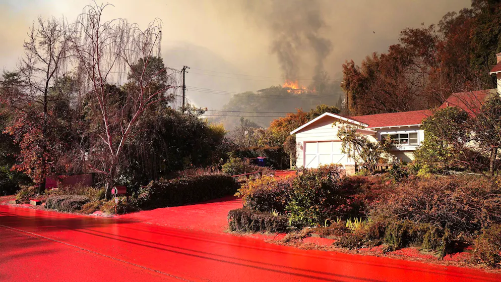Aus Flugzeugen und Helikoptern abgeworfenes Flammschutzmittel soll die Häuser in der exklusiven Mandeville Canyon Road im Stadtteil Brentwood schützen. Im Hintergrund steht ein Haus in Flammen. (11. Januar 2025