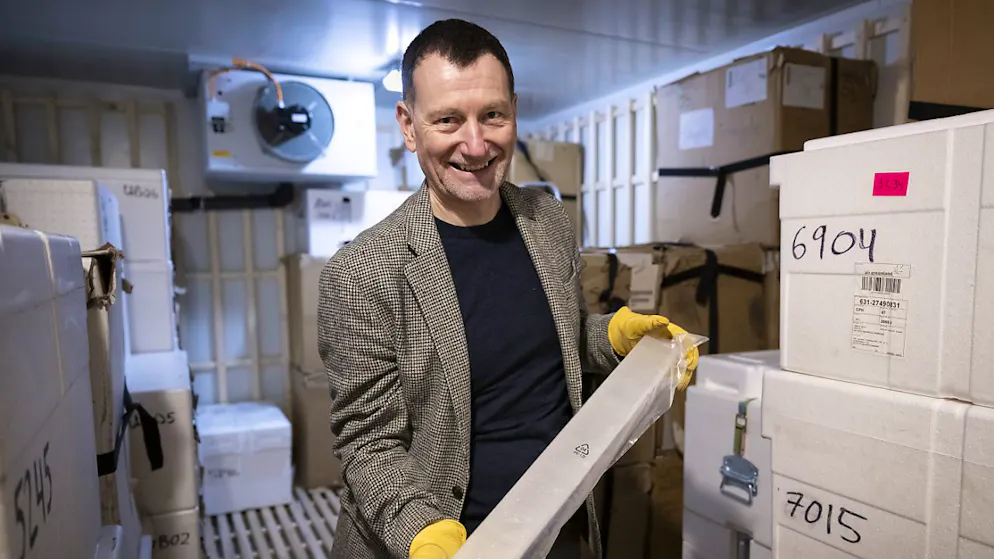Le professeur Hubertus Fischer dirige les recherches suisses. Sur la photo, il pose avec un échantillon de la calotte glaciaire du Groenland dans la chambre froide.