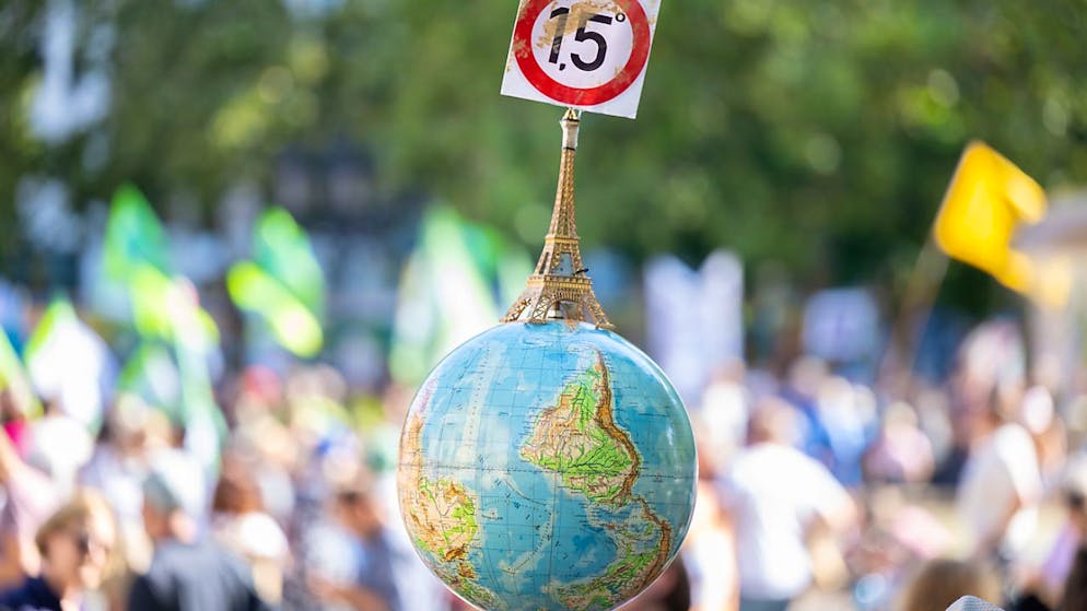 ARCHIV - Einen Globus mit einem Miniatur-Eiffelturm und dem 1,5-Grad Ziel des Pariser Klimaschutzabkommens trägt ein Mann auf der Demonstration vor der Alten Oper in Frankfurt. Foto: Boris Roessler/dpa