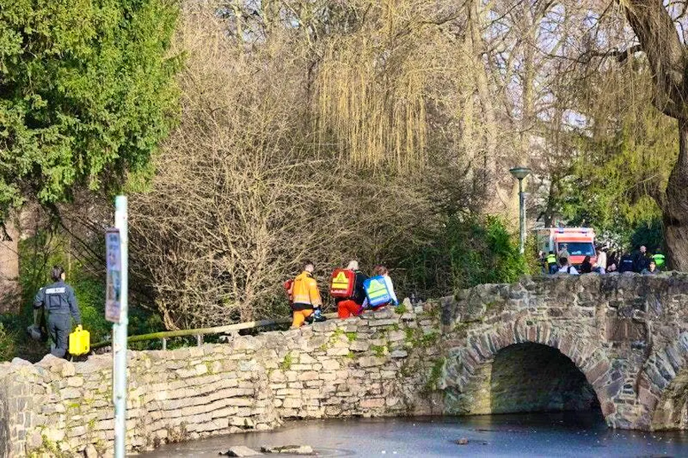 Rescue workers and forensic technicians walk up a small bridge near a crime scene.