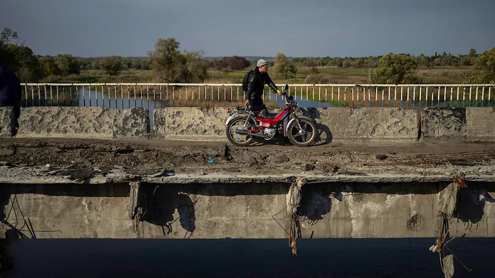 ARCHIV - Ein Mann zieht sein Motorrad auf einer zerstörten Brücke über den Fluss Oskil (Archivbild). Foto: Evgeniy Maloletka/AP/dpa