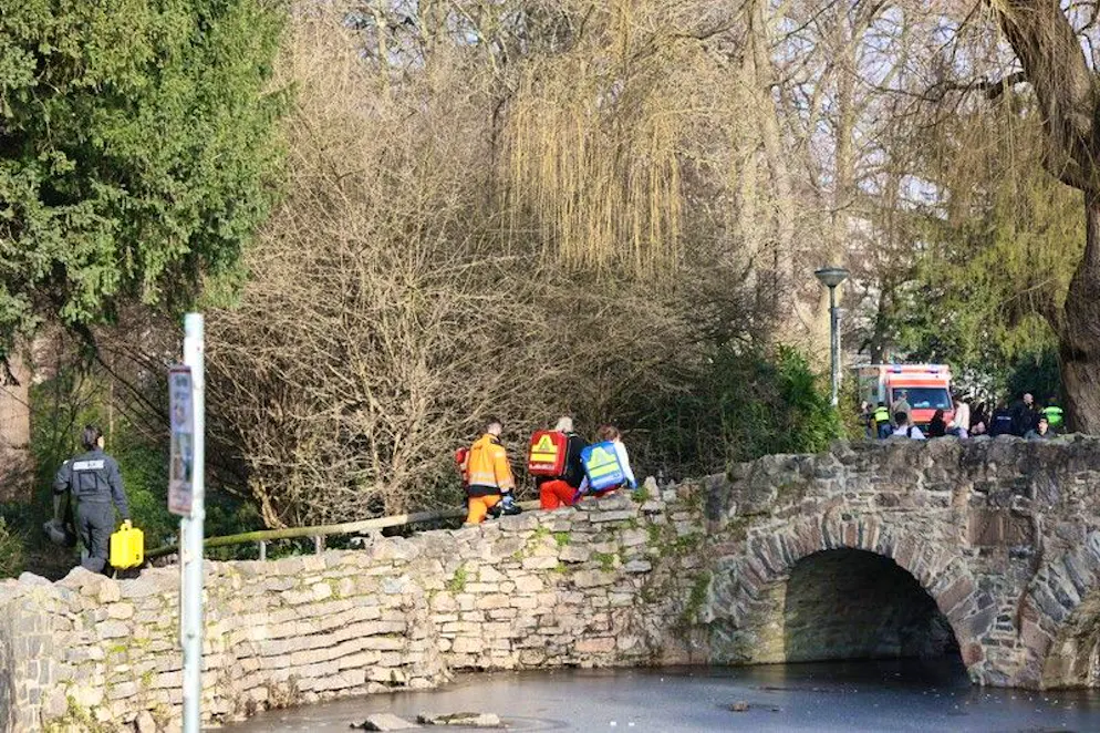  Rettungskräfte und Kriminaltechniker gehen in der Nähe eines Tatortes eine kleine Brücke hinauf.