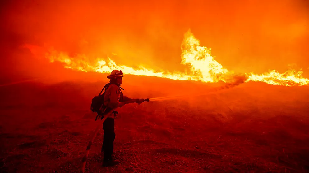 dpatopbilder - Ein Feuerwehrmann versprüht Wasser, während er die vom Hughes-Feuer verursachten Flammen an einem Straßenrand überwacht. Foto: Ethan Swope/AP/dpa