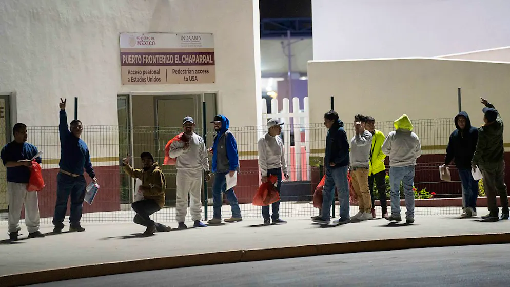 Migranten, die aus den USA abgeschoben wurden, stehen am späten Abend auf der Fußgänger-Grenzbrücke El Chaparral in Tijuana, Mexiko. Foto: Felix Marquez/AP/dpa