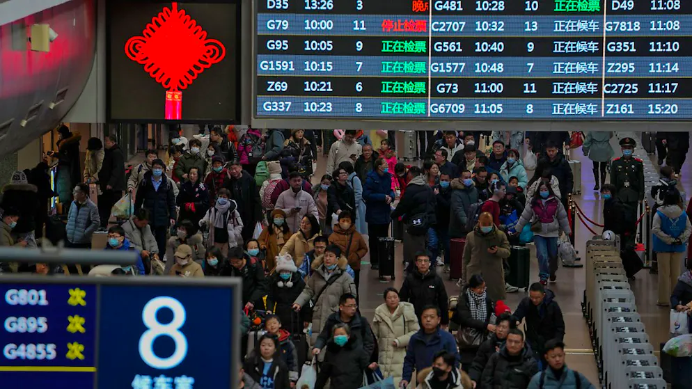 ARCHIV - Reisende gehen unter einer Zugabfahrtstafel entlang, um ihre Züge zu erreichen. Das chinesische Neujahr feiern viele Familien zusammen. Dafür reisen oft Millionen von Menschen in ihren Heimatort. Foto: Andy Wong/AP/dpa/Archivbild