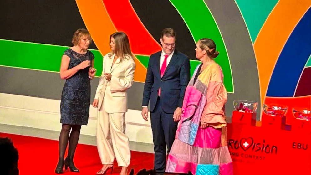 Carina Nilsson, President of the Parliament of Malmö (left), hands over the ESC "key" (on the right in the form of a cape) to the President of the Government of Basel, Conradin Cramer. In between, presenter Jennifer Bosshard.