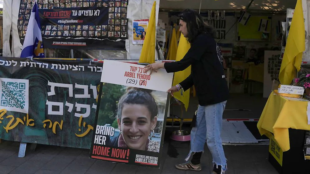 Ein Mann stellt am Eingang eines Zeltes  ein Foto von Arbel Yehud neben ein hebräisches Transparent, das die Rückkehr der von der Hamas im Gazastreifen festgehaltenen Geiseln fordert. Die Terrororganisation Palästinensischer Islamischer Dschihad hat am 27. Januar eine Videoaufnahme der deutsch-israelischen Geisel Arbel Yehud veröffentlicht. Sie soll am Donnerstag freikommen. Foto: Mahmoud illean/AP/dpa