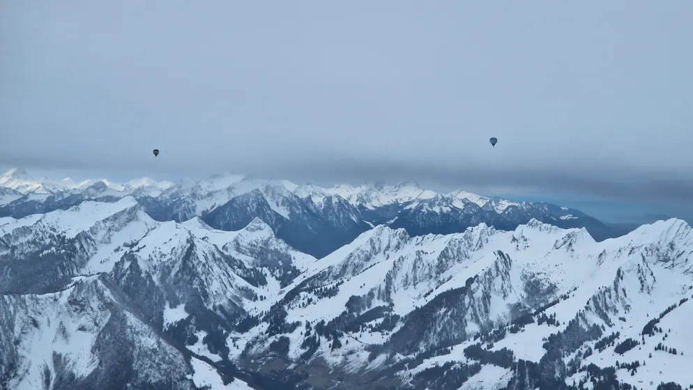 Ballons. Deux montgolfières au-dessus des cimes enneigées.