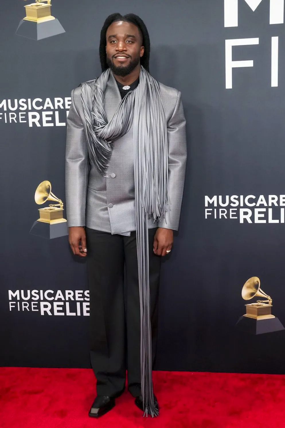 Grammy Awards 2025 – Red Carpet. Shaboozey bricht den Stil der klassischen Anzugsjacke mit Hahnentrittmuster durch einen überlangen gefransten Schal.