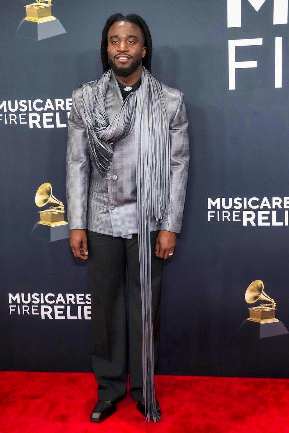 Grammy Awards 2025 - Red Carpet. Shaboozey breaks the style of the classic houndstooth suit jacket with an extra-long fringed scarf.