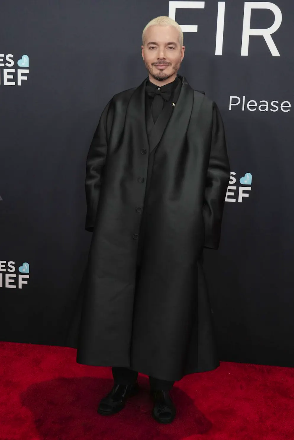 Grammy Awards 2025 – Red Carpet. J Balvin kam ganz in Schwarz, doch wählte er statt eines Anzugs einen A-Linien geschnittenen oversized Mantel. Interessant auch der Mix aus Krawatte und Fliege.