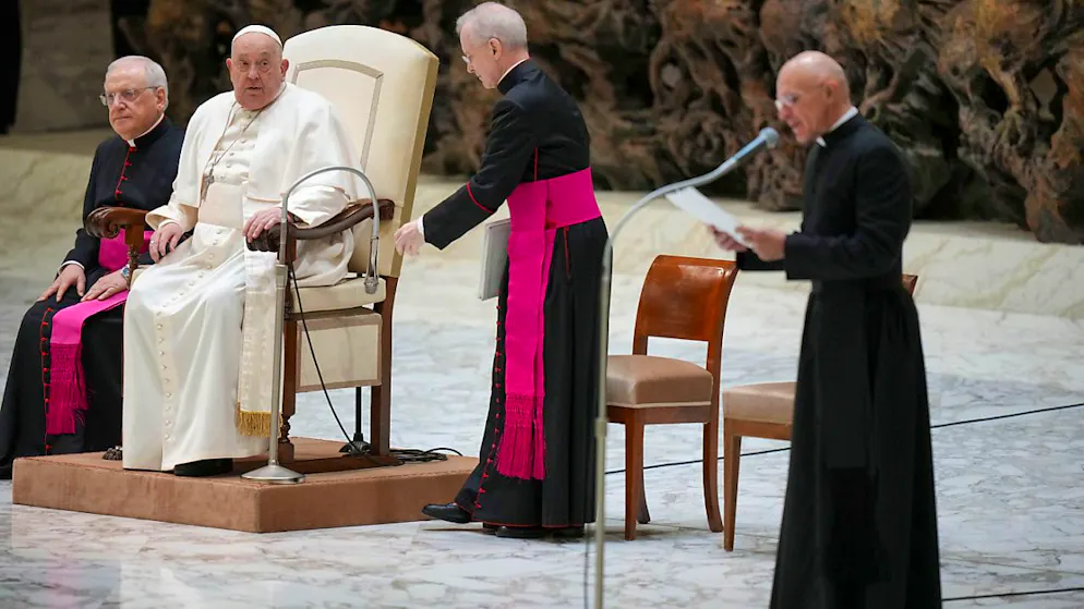 Papst Franziskus hört zu, während sein Mitarbeiter Don Pierluigi Giroli (r) seine Botschaft für ihn während der wöchentlichen Generalaudienz in der Halle Papst Paul VI. im Vatikan verliest. Der Papst bat ihn darum, da er Halsschmerzen hat. Foto: Andrew Medichini/AP/dpa
