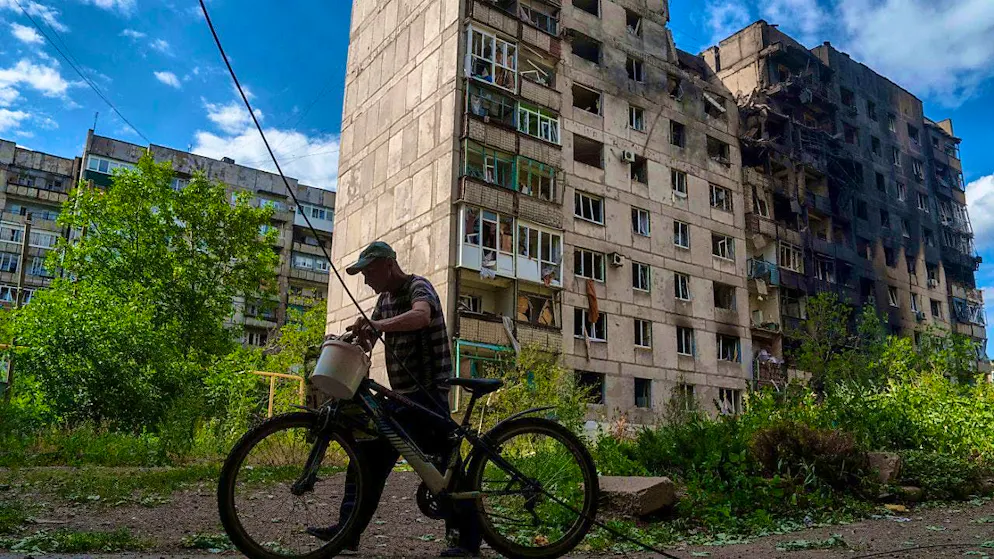 ARCHIVE - A man pushes his bicycle in front of a residential building that was destroyed by a Russian airstrike. Photo: Evgeniy Maloletka/AP/dpa