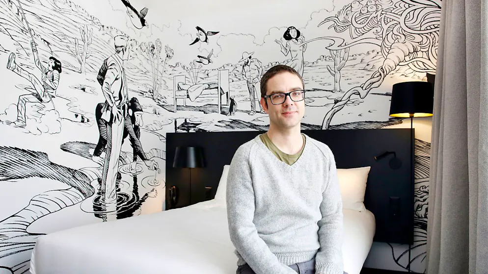 L'auteur de bande dessinée genevois Frederik Peeters, ici en 2018 dans une chambre d'hôtel dont les murs sont décorés de ses oeuvres, sera à l'honneur à Carouge jusqu'à la fin mars (archives).