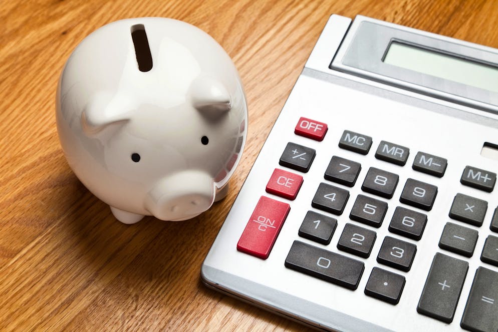 White Piggy Bank and calculator on wood table top