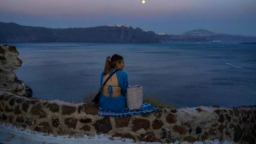 ARCHIVE - A woman looks out over the Aegean Sea as the moon rises on the island of Santorini. Photo: Petros Giannakouris/AP/dpa