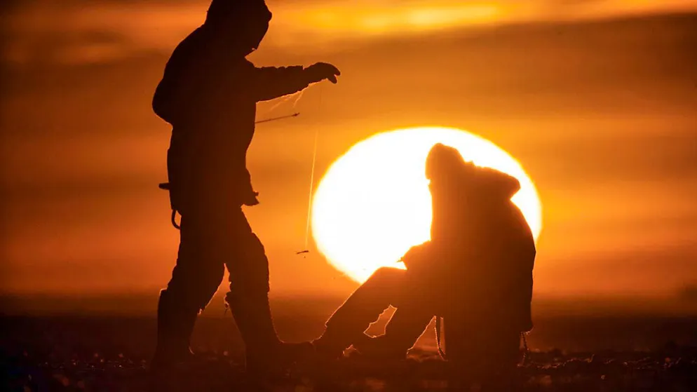 Men fishing through ice holes in the Gulf of Finland off St. Petersburg at sunset. (symbolic photo)