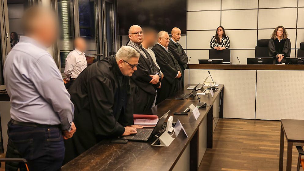 Die drei Angeklagten stehen vor der Urteilsverkündung zwischen Anwälten. Foto: Oliver Berg/dpa - ACHTUNG: Person(en) wurde(n) aus rechtlichen Gründen gepixelt