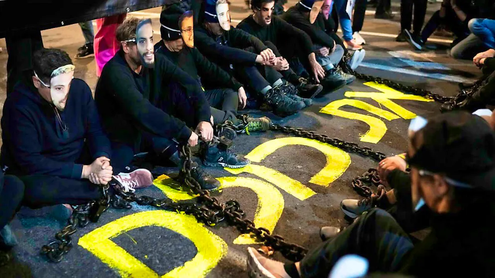 Activists sit with iron chains on a street in Tel Aviv wearing masks with the faces of hostages still being held by the terrorist organization Hamas in the Gaza Strip. Photo: Leo Correa/AP/dpa