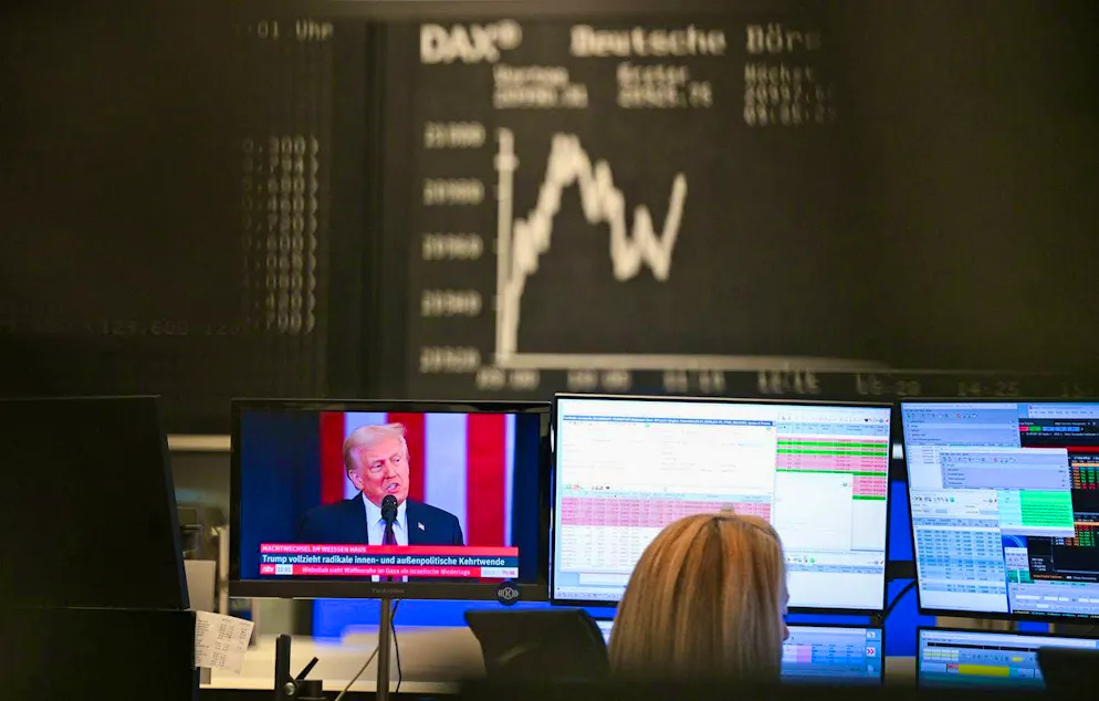 dpatopbilder - 21.01.2025, Hesse, Frankfurt/Main: The Dax curve shows upward and downward movements in the trading hall of the Frankfurt Stock Exchange, while the new US President Donald Trump can be seen on a screen. Photo: Arne Dedert/dpa +++ dpa-Bildfunk +++ (KEYSTONE/DPA/Arne Dedert)