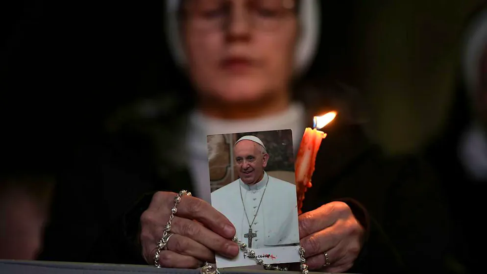 Eine Nonne hält eine Kerze und ein Bild von Papst Franziskus während eines Rosenkranzgebets für seine Gesundheit auf dem Petersplatz im Vatikan. Foto: Andrew Medichini/AP/dpa